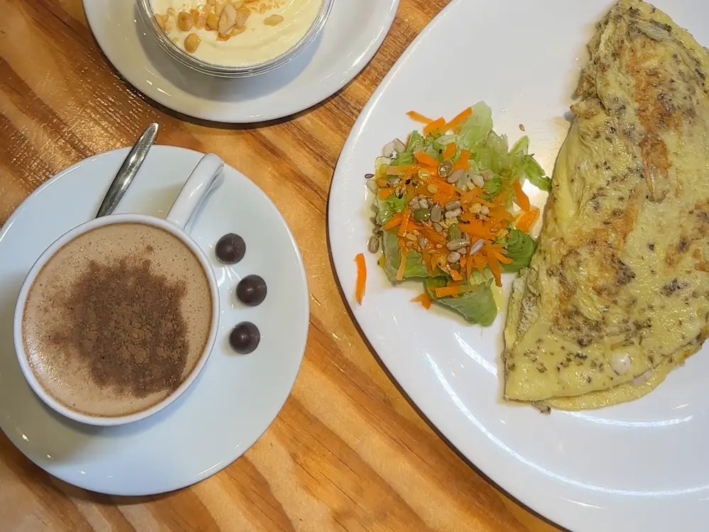 Café com cacau polvilhado, crepioca e salada na mesa da loja